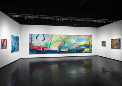 Wide installation view of the PROXYCO Gallery booth at NADA Miami 2025, without foreground furniture. The large-scale multi-panel painting Viendo el Monte Calvario by Lucía Vidales spans the center wall, flanked by smaller figurative paintings on both sides. Dark reflective floor, industrial ceiling with track lighting.